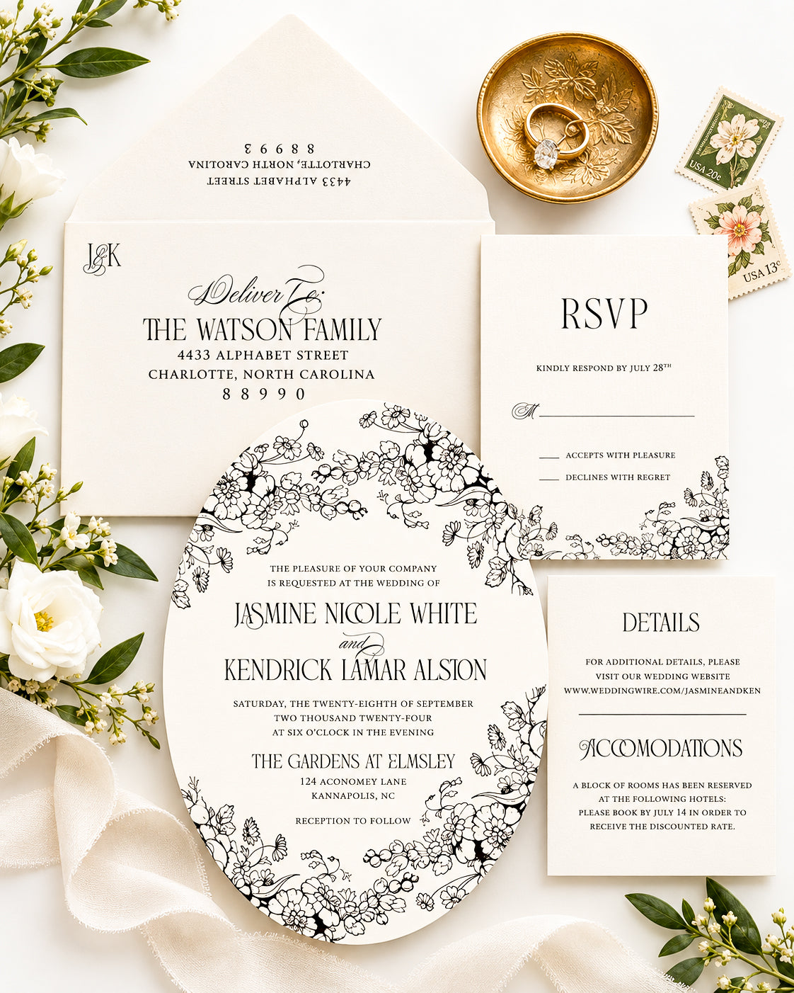 A coordinated wedding invitation suite arranged in a flat lay on a light fabric background, with floral greenery, a gold dish, rings, and small cards. The suite includes a main invitation, RSVP card, details card, and a round insert with black floral line art on white.